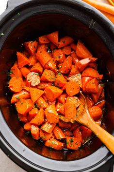 cooked carrots in a slow cooker with a wooden spoon and parsley on the side