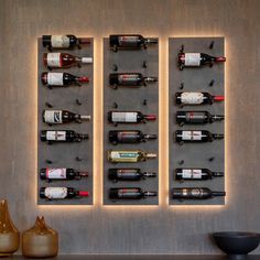 several wine bottles are lined up on the wall next to two vases and a bowl