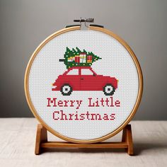 a cross stitch christmas ornament with a red car carrying a tree on top