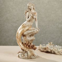 a statue of a mermaid sitting on top of a rock next to some seashells