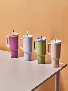 three different colored coffee cups sitting on top of a white table next to each other