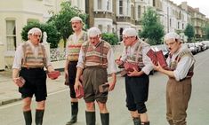 five men in traditional german clothing standing on the side of the road talking to each other