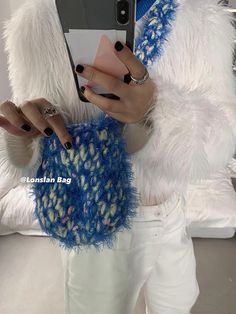 a woman holding a cell phone in her hand while wearing white pants and blue sweater