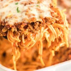 a fork full of spaghetti with meat and cheese on it, in a casserole dish