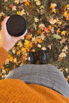 a person is holding a coffee cup in front of some autumn leaves on the ground