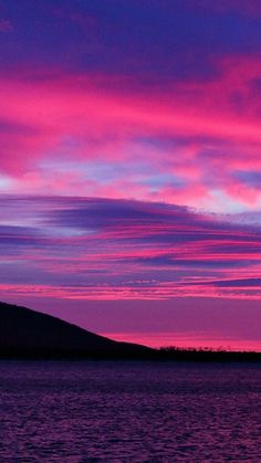 the sky is pink and purple as it sits on top of a hill over water