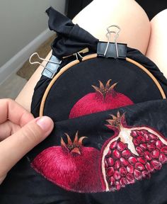 a woman is showing off her embroidered pomegranates on the back of her purse