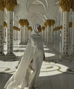 a woman in a white outfit is walking through an ornate room with columns and chandeliers