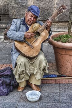 a man sitting on the ground playing a guitar next to a potted planter