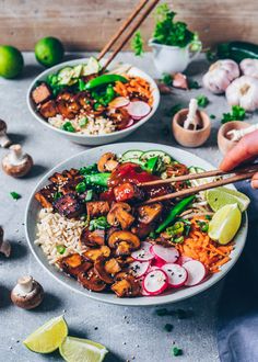 someone holding chopsticks over a plate of food with mushrooms, rice and vegetables