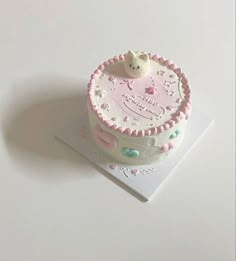 a pink and white birthday cake with a teddy bear on top, sitting on a card