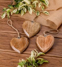 three heart shaped wooden ornaments hanging from twine strings on a table with greenery