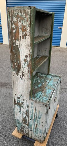 an old wooden cabinet sitting on top of a pallet next to a blue garage door