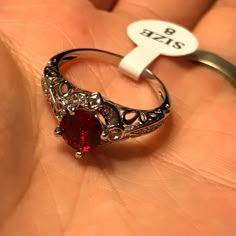 a close up of a person's hand holding a ring with a red stone