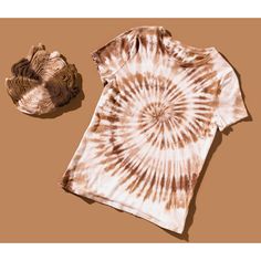 a brown and white tie dye shirt next to a hat on top of a tan background