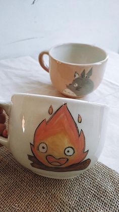 two cups with faces painted on them sitting next to each other, one has an orange flame in the middle