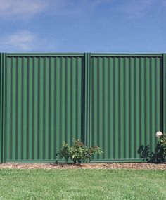 a large green metal fence in the middle of a grassy area next to some flowers