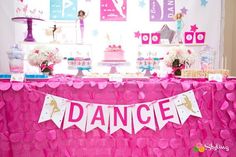 a pink table topped with lots of cake and desserts next to a wall covered in paper hearts