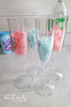 three wine glasses filled with different colored liquid and cotton floss next to a bottle of booze