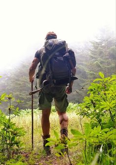 a man with a backpack and trekking poles walks through the woods