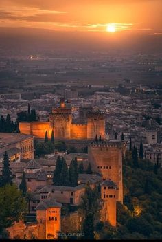 the sun is setting over an old city and its castle like structures are lit up