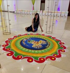 a woman is sitting on the floor in front of a colorful rangolite design