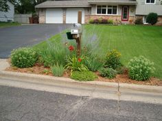 a mailbox sitting in the middle of a flower bed next to a driveway and house