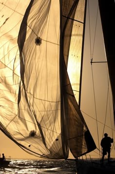 two people on a sailboat in the ocean with sails down and one person standing at the front of the boat