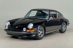 an old black porsche sits parked in a room with gray walls and white flooring