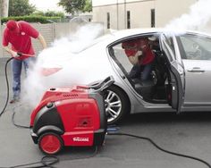 a man in red shirt washing a car with a high pressure washer and hose