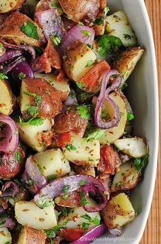 a white bowl filled with potatoes, onions and other vegetables on top of a wooden table