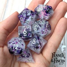 purple and silver dice with numbers on them in someone's hand that is holding it