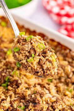 a spoon full of rice and meat in a casserole dish with green onions