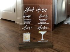 a glass sign with different types of drinks on it sitting in front of a refrigerator