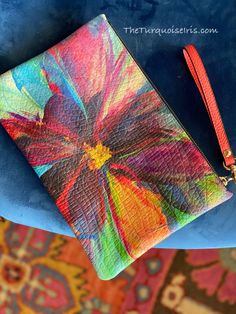 a colorful wallet sitting on top of a blue chair next to a rug with an orange tassel