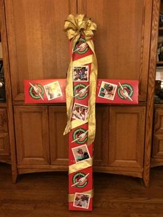 a wooden cross with pictures on it and a ribbon tied around the cross is sitting in front of a cabinet