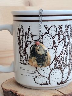 a white coffee cup with a rock hanging from it's side on a chain