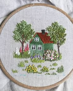 a green house surrounded by flowers and trees on a gray background with a wooden hoop