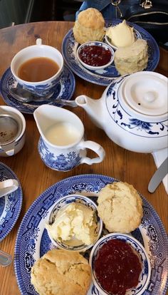 an assortment of biscuits and jams sitting on a table with tea cups, saucers and spoons