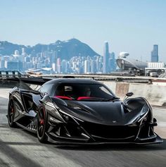 a black sports car driving down the road in front of a large cityscape