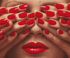 a woman's face with her hands over her eyes and red nail polish on it