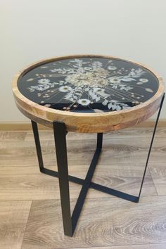 a round table with flowers painted on the top and black metal legs, in front of a white wall