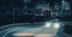 a car driving down a city street at night with the lights on and buildings in the background