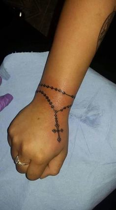 a person with a cross tattoo on their wrist holding onto a rosary bracelet that is attached to the wrist