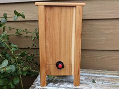 a wooden box with a red light on it sitting in front of a house next to a bush