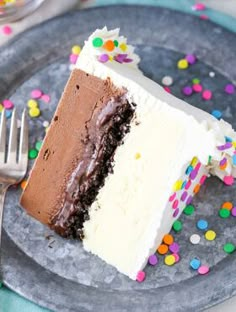 a slice of chocolate cake with white frosting and sprinkles on a plate