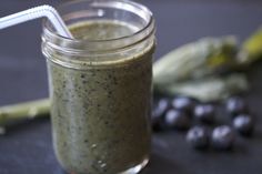 a glass jar filled with green smoothie next to blueberries