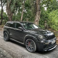 a black jeep parked on the side of a road next to some trees and bushes