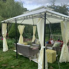 a white gazebo sitting in the middle of a lush green field with lots of furniture