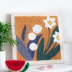 a watermelon sits next to a crocheted wall hanging